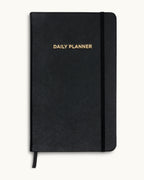 Front cover of the black Matine Daily Planner with gold “DAILY PLANNER” embossing, elastic band, and ribbon bookmark.