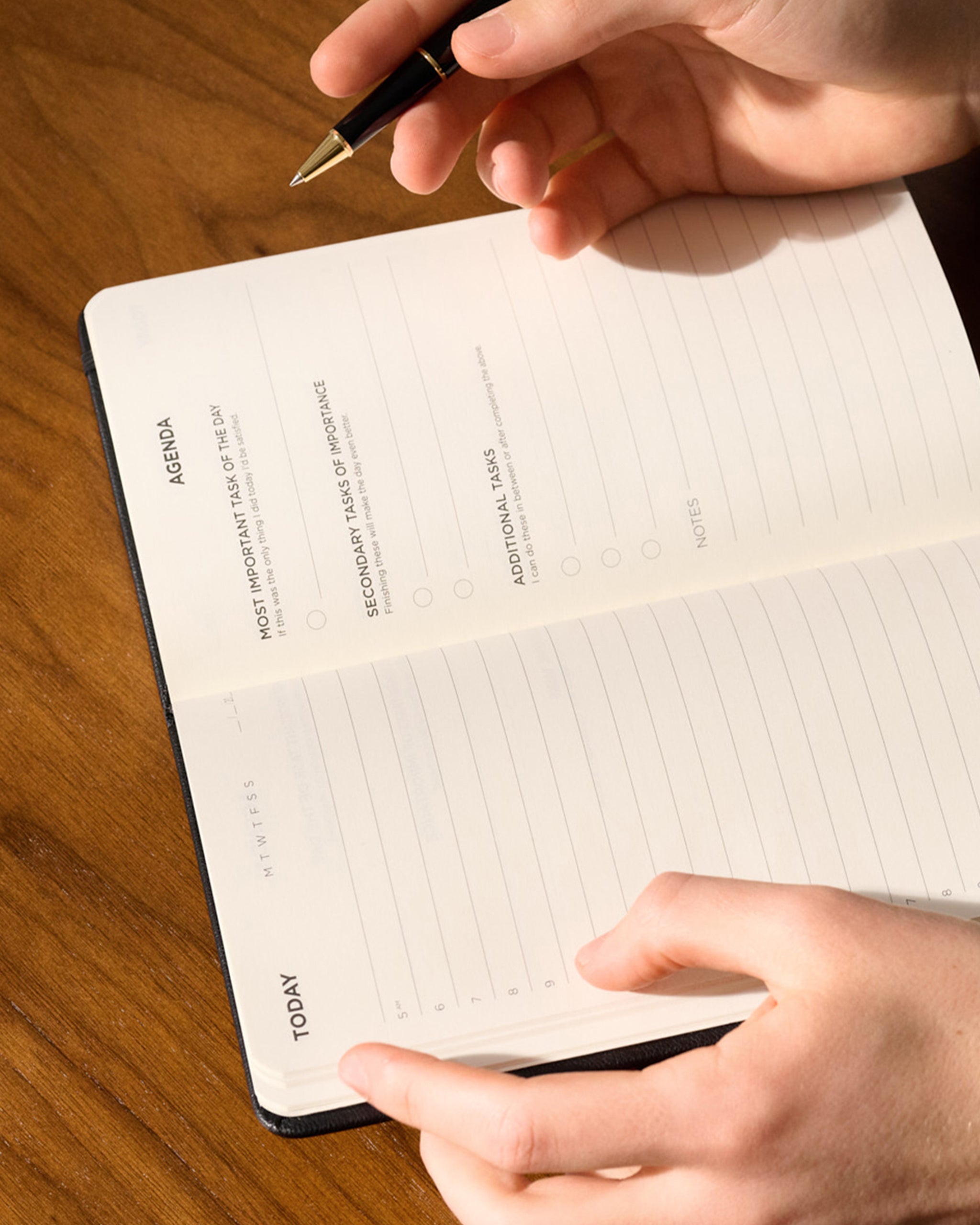Hands writing in an open daily planner on a wooden table.
