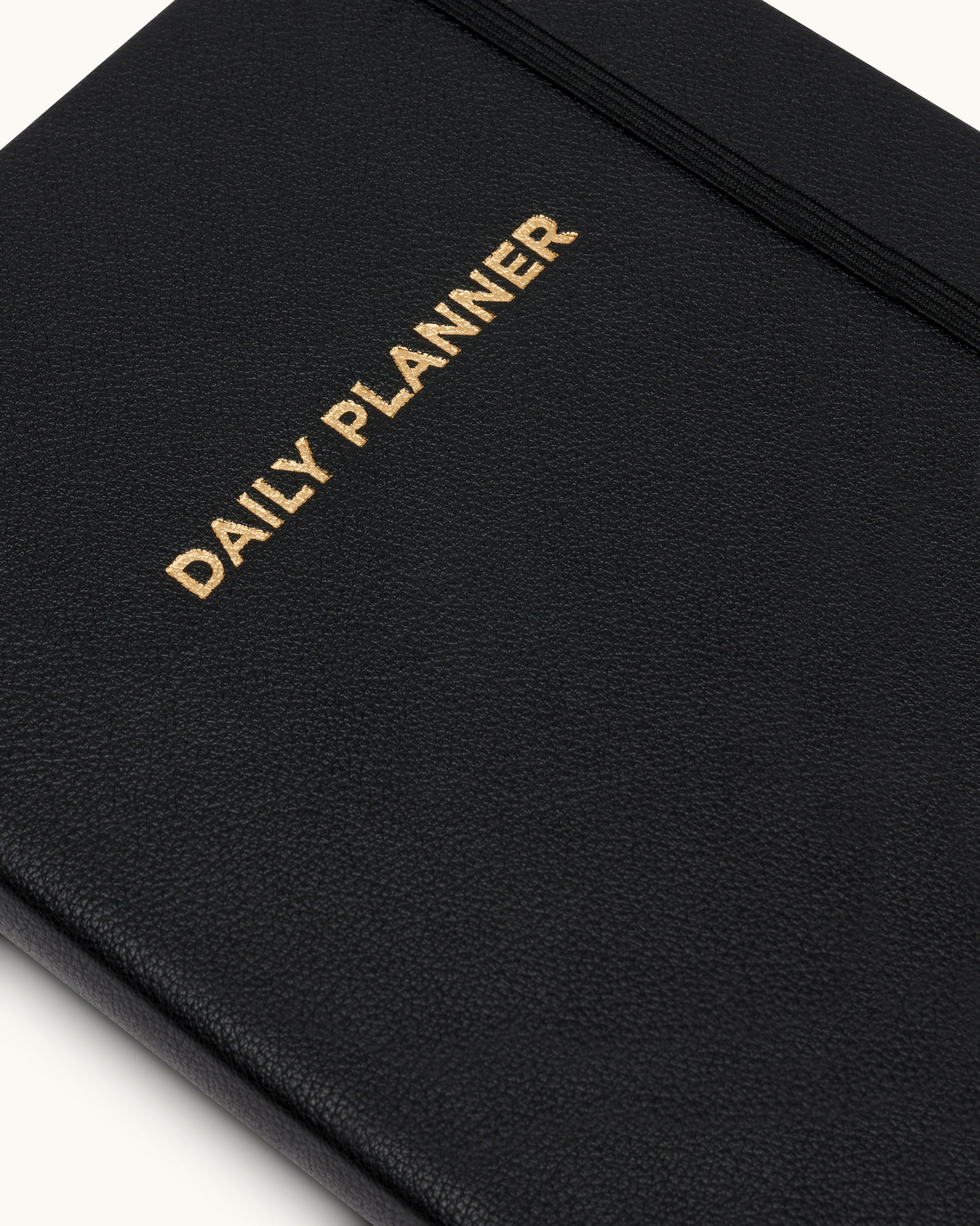 Close-up of the black Matine Daily Planner cover with gold “DAILY PLANNER” embossing, textured surface, and black elastic band.