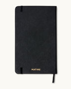 Back cover of the black Matine Daily Planner with gold “MATINE” embossing, elastic band, and ribbon bookmark visible.