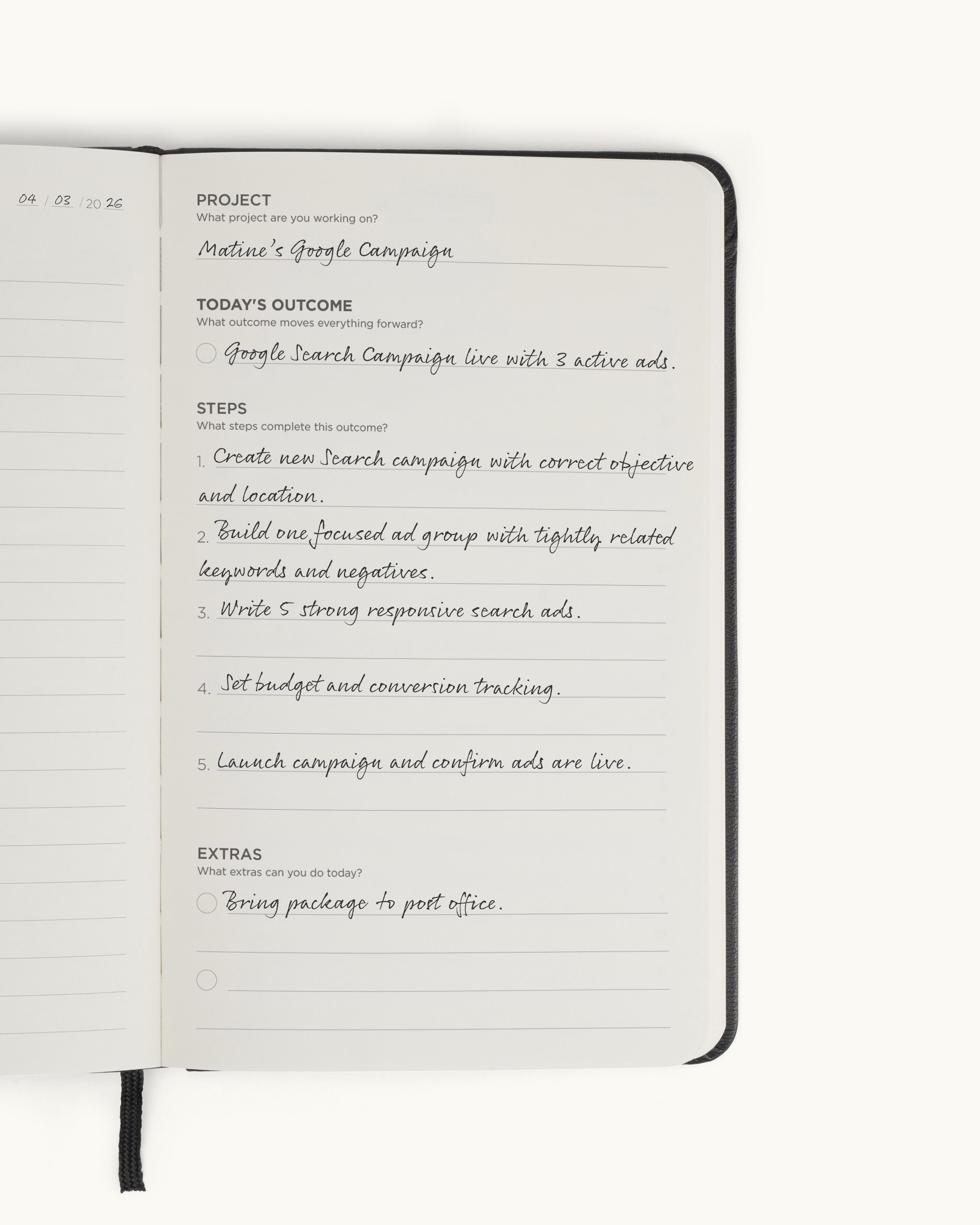 Open spread of the black Matine Daily Planner showing the filled “Project,” “Today’s Outcome,” “Steps,” and “Extras” page with handwritten entries and ribbon bookmark visible.