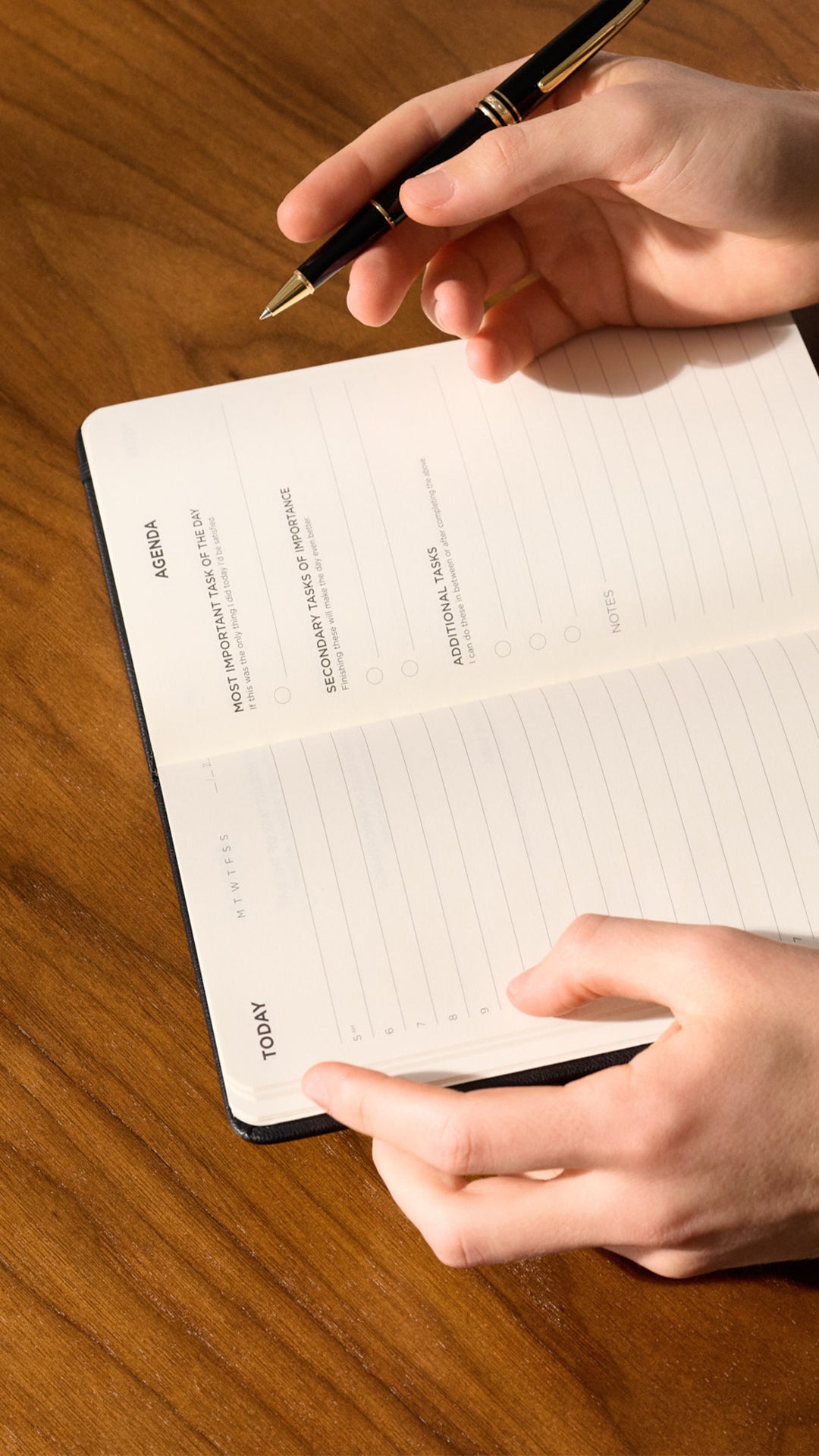 Hands writing in an open daily planner on a wooden table.