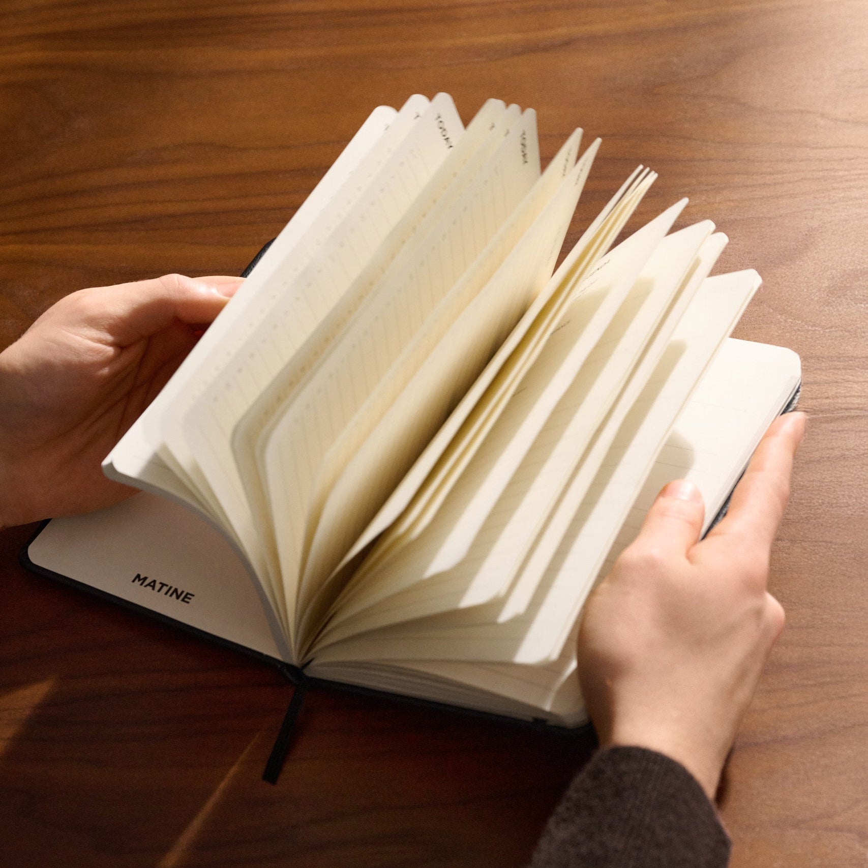 Person blättert durch die Seiten eines offenen Daily Planners auf einem Holztisch.